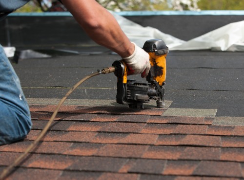 Roofer uses gun to lay shingles while doing chimney flashing and repair in Fairbury, IL