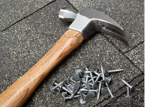 A hammer and nails are seen on a roof. If you wonder, "What do I do if my roof is damaged by hail?" call Popejoy Roofing.