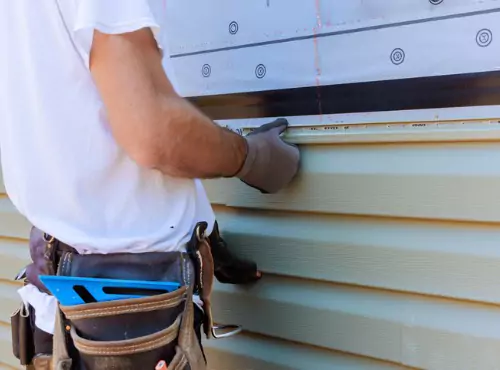 A man is seen installing siding. Popejoy Roofing is the best of the Siding Companies.